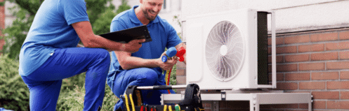 HVAC technician in navy-blue uniform inspecting an outdoor AC unit beside a brick house in a suburban neighborhood.